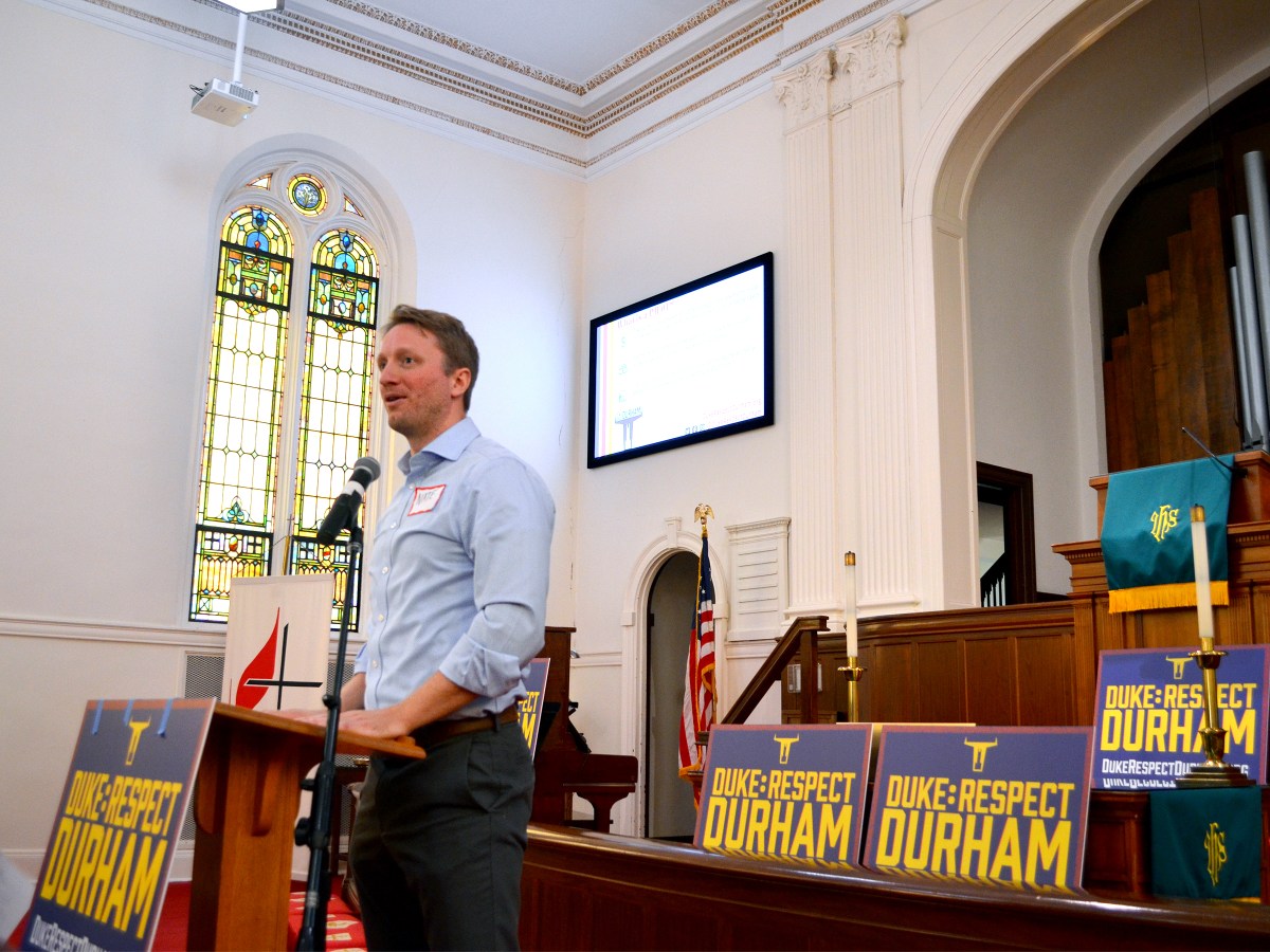 A man stands at a lectern in front of signs